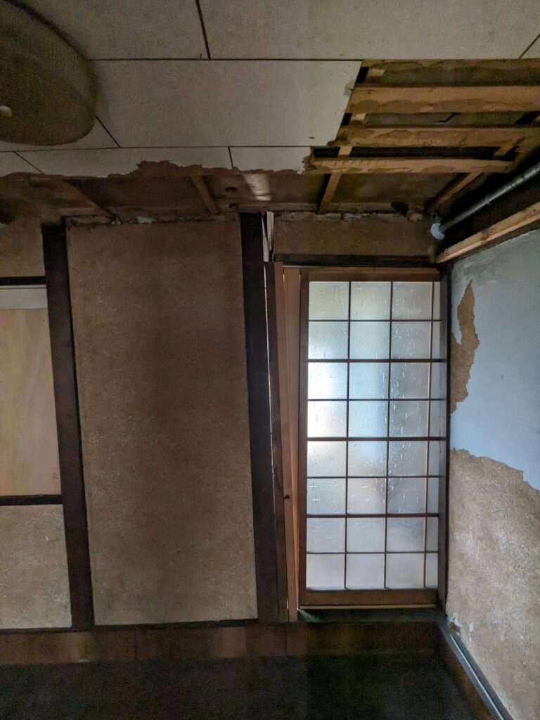 天井や壁が大きく損傷した室内。天井板が剥がれ下地が見え、壁の砂壁も崩れているなど、老朽化が進んだ空き家の状態が分かる。