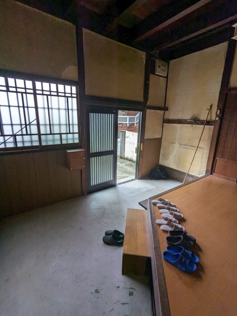 古い空き家の玄関土間の様子。壁や天井に劣化が見られ、割れたコンクリート。