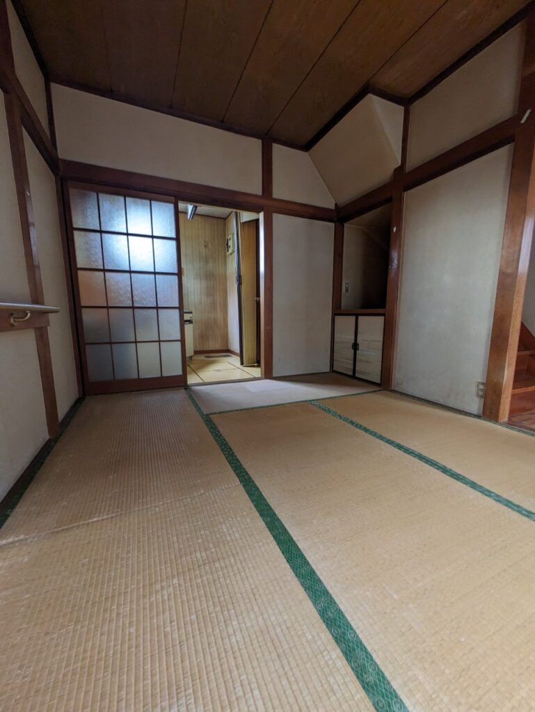 経年劣化が見られる和室の室内。畳が傷んだ床と木枠の障子があり、奥の部屋へ続く引き戸や収納スペースが見える。