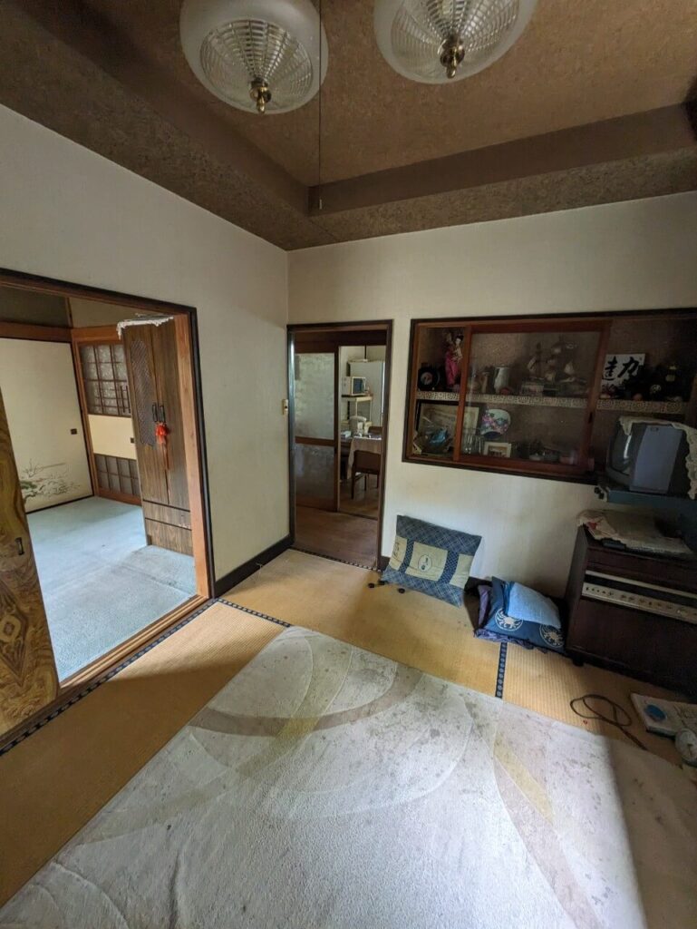 畳の傷みや古い家具の残置物があり、続き間の部屋の様子が分かる、空き家の和室内部を写した写真