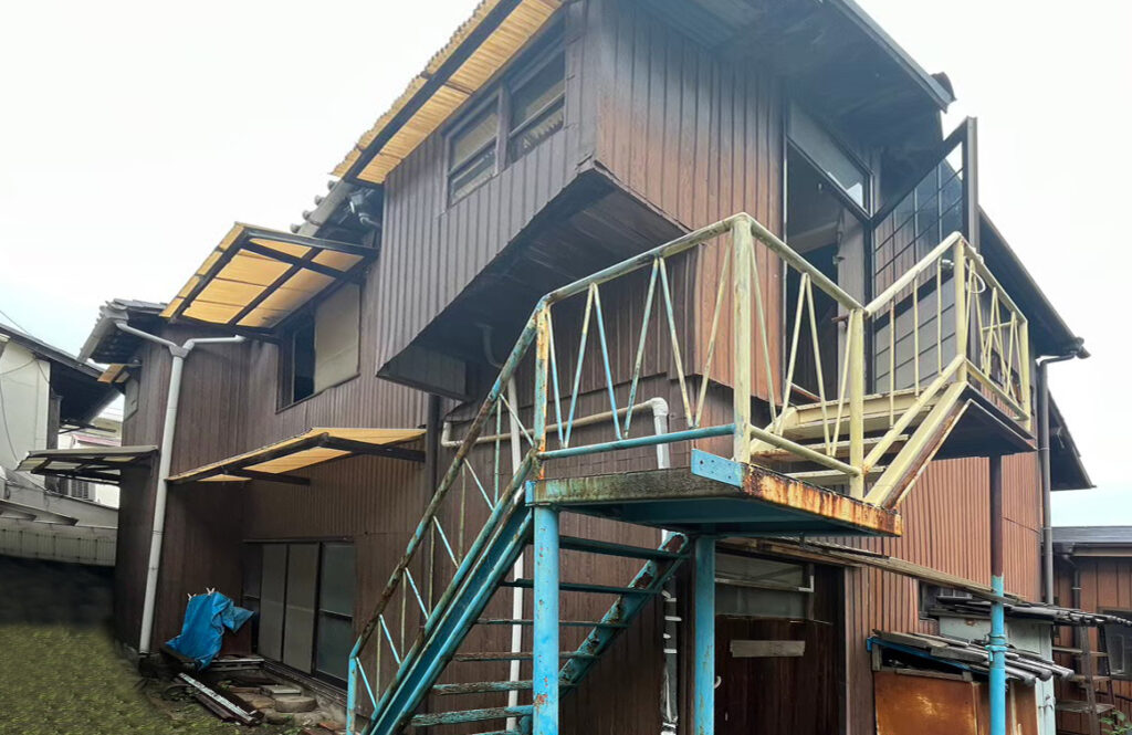 神戸市で共有持分を買取した空き家の外観。老朽化が進んだ木造住宅で、錆びた鉄製階段や傷んだ外壁が目立つ状態。