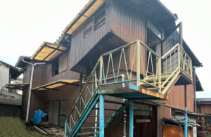 神戸市で共有持分を買取した空き家の外観。老朽化が進んだ木造住宅で、錆びた鉄製階段や傷んだ外壁が目立つ状態。