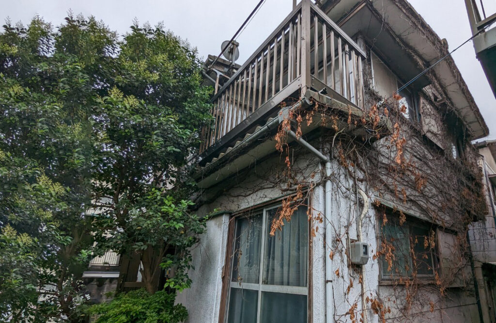 横浜市中区竹之丸で5年間放置されていた再建築不可物件の外観。つたが絡まり外壁に劣化が見られ、バルコニーや窓周りが老朽化した状態の戸建。