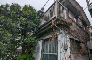 横浜市中区竹之丸で5年間放置されていた再建築不可物件の外観。つたが絡まり外壁に劣化が見られ、バルコニーや窓周りが老朽化した状態の戸建。